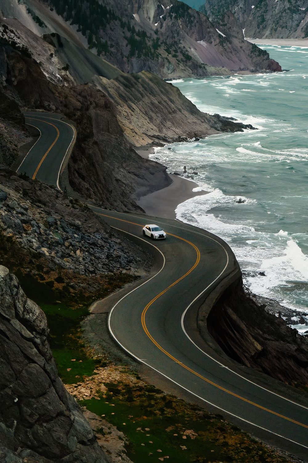 White car on a twisting coastal road above the surf