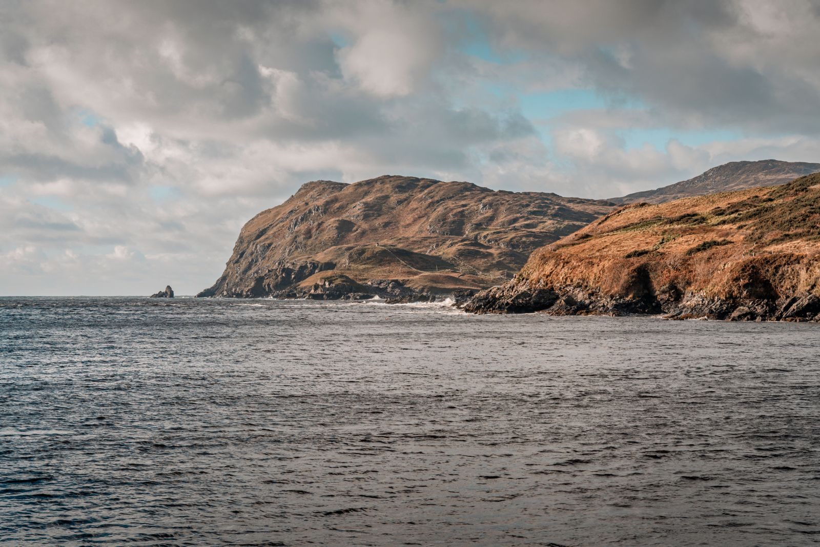 Rugged headland and sea cliffs under heavy clouds on the coast of Ireland, scenery seen on private driver tours of Ireland