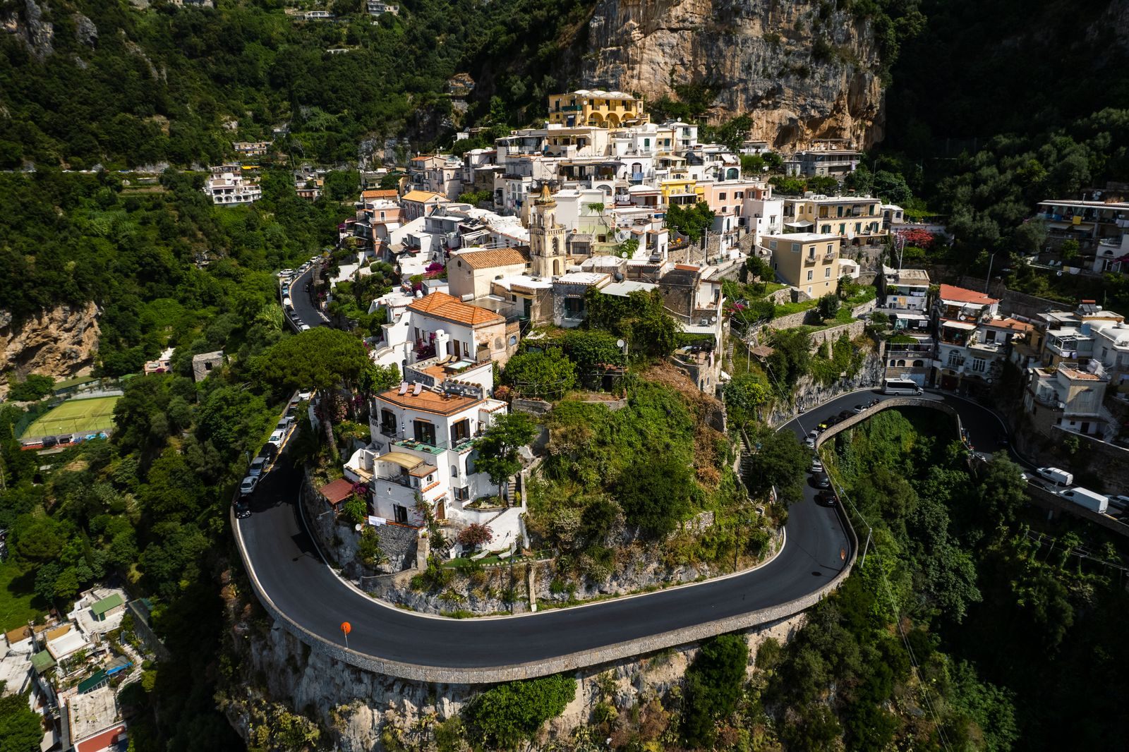 Aerial view of a hillside village on the Amalfi Coast with the coast road wrapping around it in a hairpin, a classic route when you hire a private driver in Italy