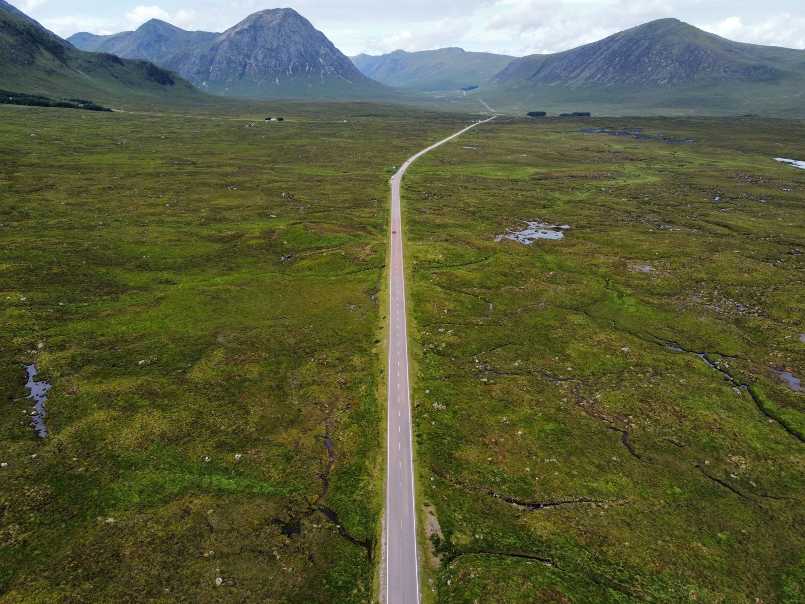 Straight road crossing open moorland toward the mountains of Glen Coe, a highlight of private driver tours in Scotland