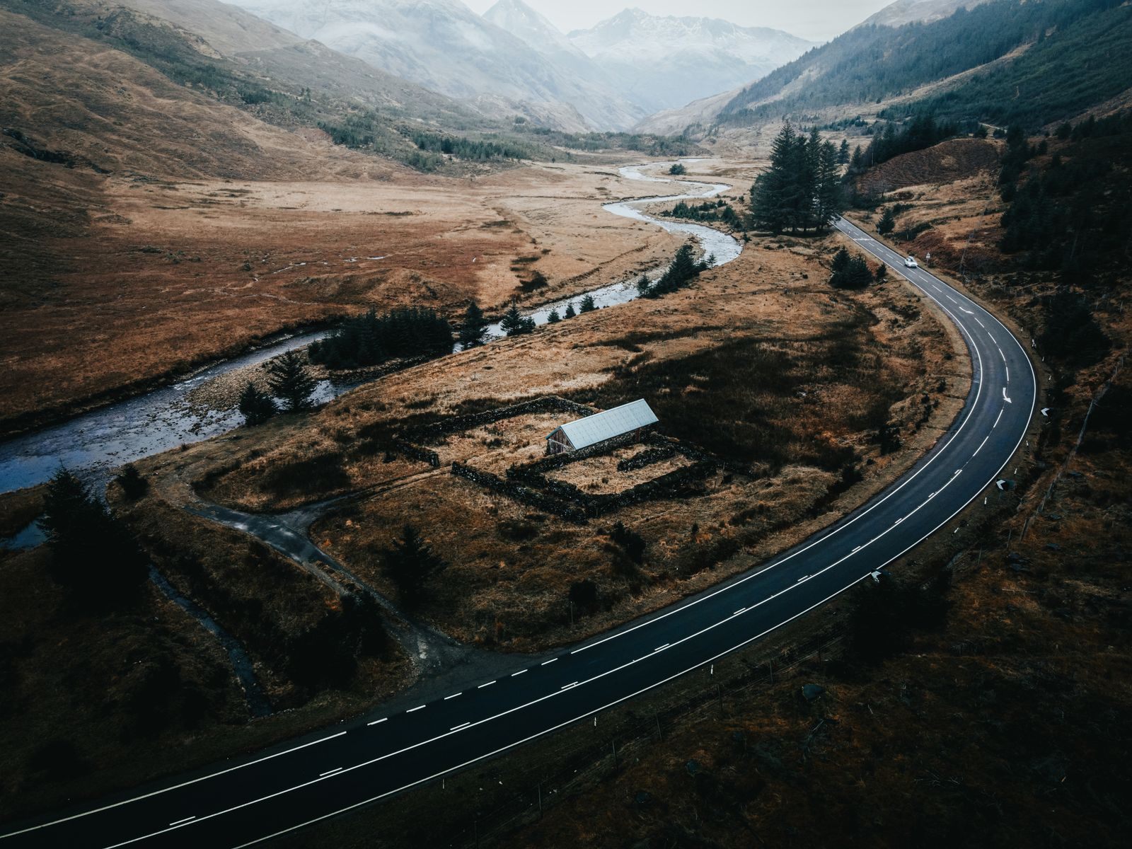 Aerial view of a two-lane road curving beside a river through brown Highland moorland in Scotland